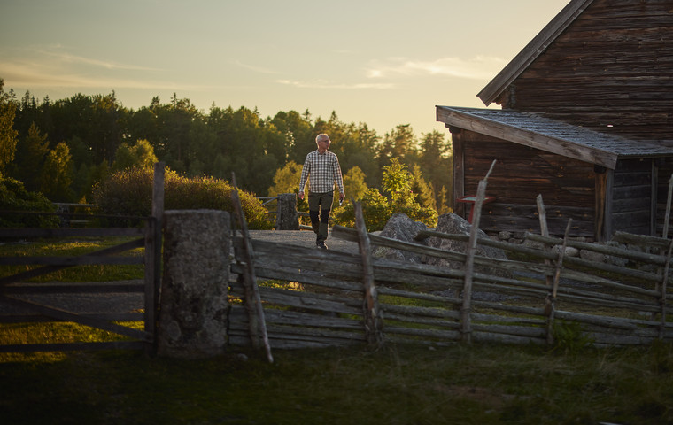 Person går vid en äldre ladugård, i förgrunden står en gärdsgård. Foto: Patrik Svedberg