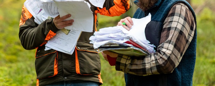 Två personer som står med mängd pappersblanketter mitt i skogen. Foto: Bulldozer