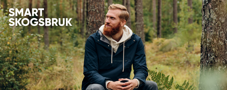 En skäggprydd medelålders man i jeans, jacka och luvtröja sitter på en mossbeklädd sten i en tallskog och tittar förnöjsamt på sin skog. I händerna håller han en kaffemugg. Han tänker och ser tillfreds ut, som om han tagit ett smart beslut. I hörnet på bilden står texten "Smart Skogsbruk".