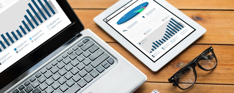 Close up of on laptop computer and tablet with charts, and eyeglasses on a wooden table. Foto: lev dolgachov