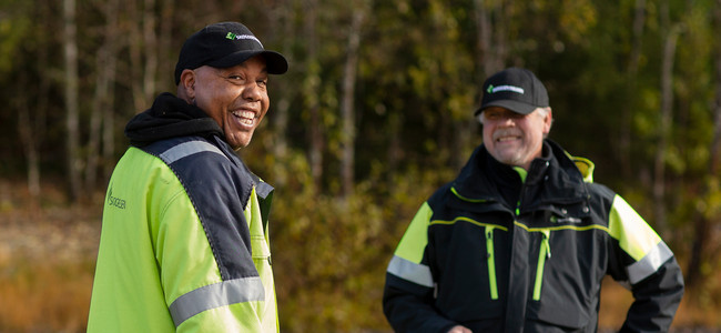 Två glada men med keps med skog i bakgrunden. Foto: Malin Grönborg
