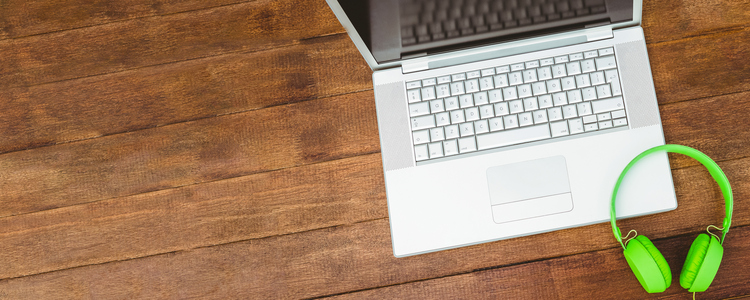 View of a grey laptop with a green headphone on wood desk. Foto: Wavebreak Media LTD