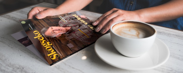 Kvinna öppnar tidningen Skogseko över en bordsskiva med en stor kopp kaffe bredvid sig.