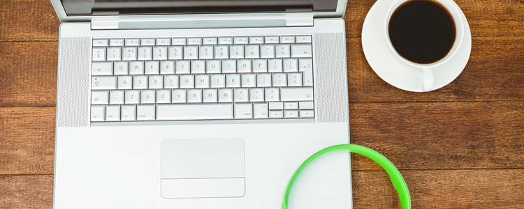 View of a grey laptop with a green headphone on wood desk. Foto: MostPhotos