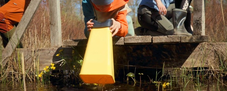 Några barn sitter på en brygga. Ett av barnen använder en gul vattenkikare