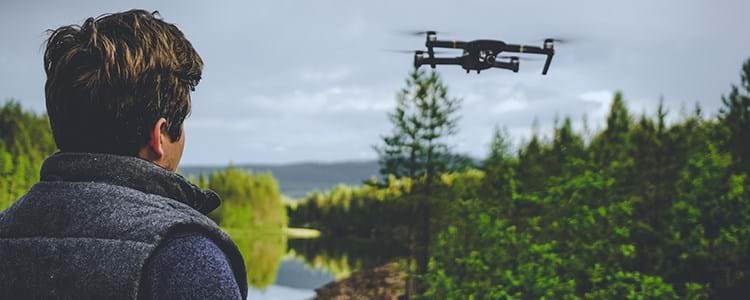 En drönarpilot som flyger lågt med en drönare över skog och vattendrag i norra Sverige.