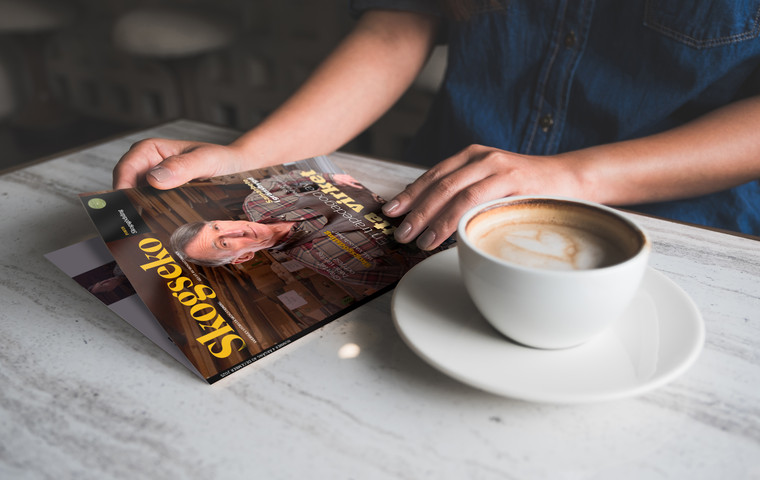Kvinnohänder som öppnar senaste numret av Skogseko på bordsskiva med kaffekopp bredvid sig.