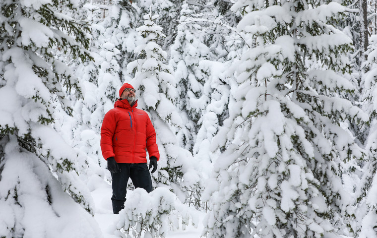 Man i röd dunjacka och mössa står mitt inne bland snötäckta granar. Ett riktigt vinterlandskap. Foto: André Nyström