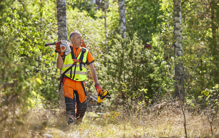 Man som går genom skogen med röjsåg på axeln. Foto: Patrik Svedberg