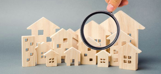 Minimodeller av hus utsågade i trä. En hand med förstoringsglas zoomar in på ett av husen.