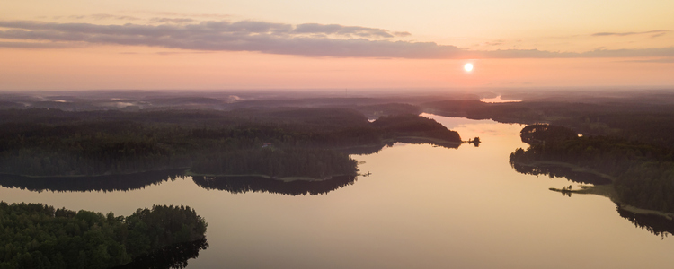 Vy över sjö och skog i rosa kvällsljus. Foto: Mostphotos