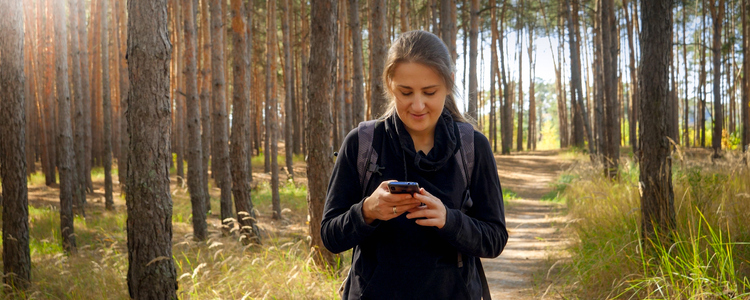 Ung kvinna som går i skogen, tittar ner på sin mobiltelefon.
