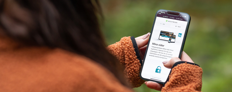 Närbild på kvinna i fleecejacka som tittar på sin mobiltelefon i skogen. På mobilen syns inloggningssidan till Skogsstyrelsens Mina Sidor. Foto: Bulldozer