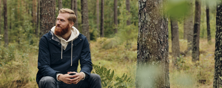 En skäggprydd medelålders man i jeans, jacka och luvtröja sitter på en mossbeklädd sten i en tallskog och tittar förnöjsamt på sin skog. I händerna håller han en kaffemugg. Han tänker och ser tillfreds ut, som om han tagit ett smart beslut.