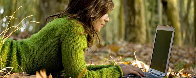 Kvinna som ligger ner och skriver på en dator i skogen.