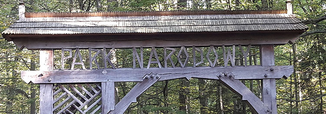 A wooden sign at an entrance to a park saying "Park Narodowy".