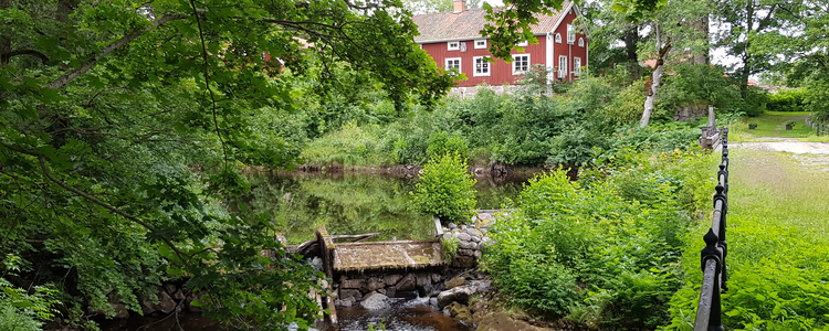 Summer environment from Järle Kvarn with rushing river, lush trees and older red houses with white knots. Foto: Göran Lundh