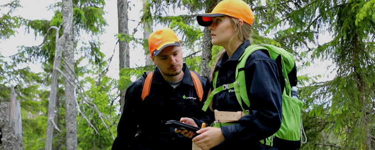 Två studenter, en man och en kvinna, står i skogen och planerar dagens arbete.